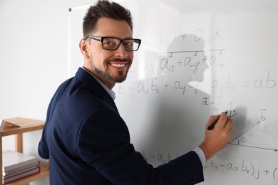 Photo of Happy teacher explaining mathematics at whiteboard in classroom