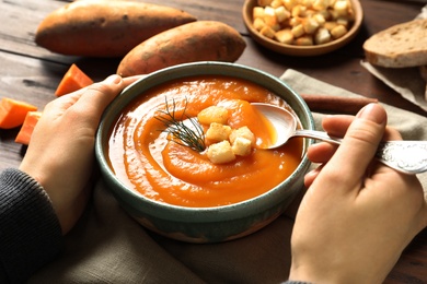 Photo of Woman eating tasty sweet potato soup at table, closeup