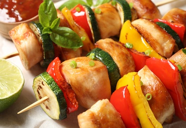 Photo of Delicious chicken shish kebabs with vegetables and lime on parchment, closeup