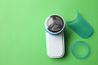 Photo of Modern fabric shaver and parts on green background, flat lay. Space for text