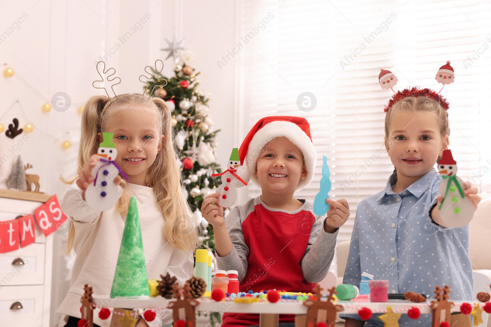 Photo of Cute little children with beautiful Christmas crafts at table decorated in room