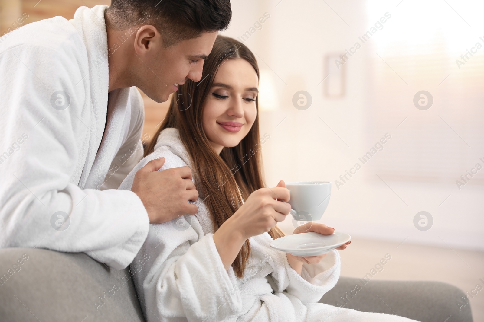 Photo of Man in bathrobe hugging his girlfriend with coffee at home