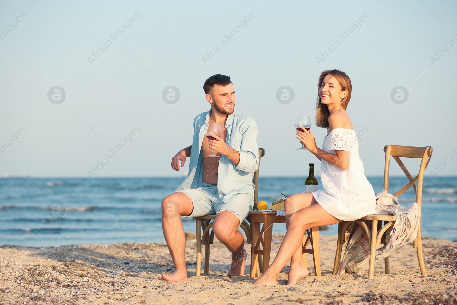 Photo of Young couple with glasses of wine having romantic dinner on beach