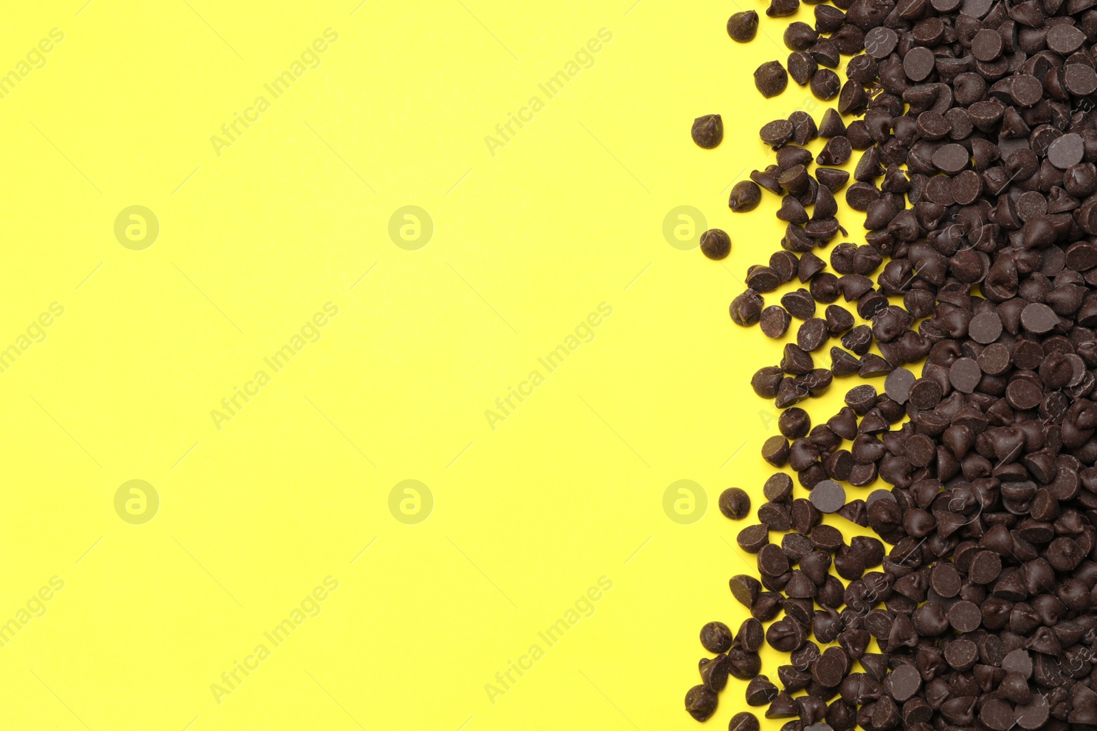 Photo of Pile of delicious dark chocolate chips on yellow background, top view. Space for text