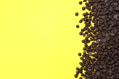 Photo of Pile of delicious dark chocolate chips on yellow background, top view. Space for text