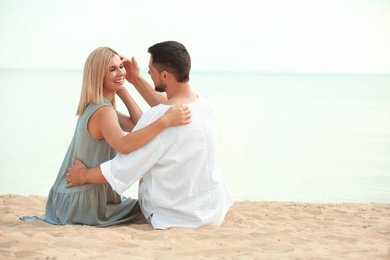 Photo of Happy romantic couple sitting on beach, space for text
