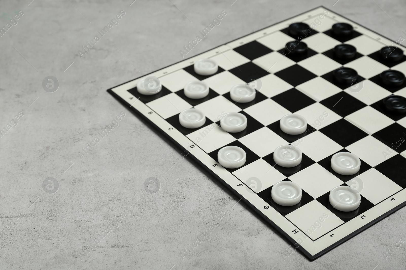 Photo of Checkerboard with game pieces on light grey table. Space for text