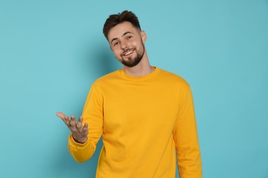 Handsome man in yellow sweatshirt gesturing on light blue background
