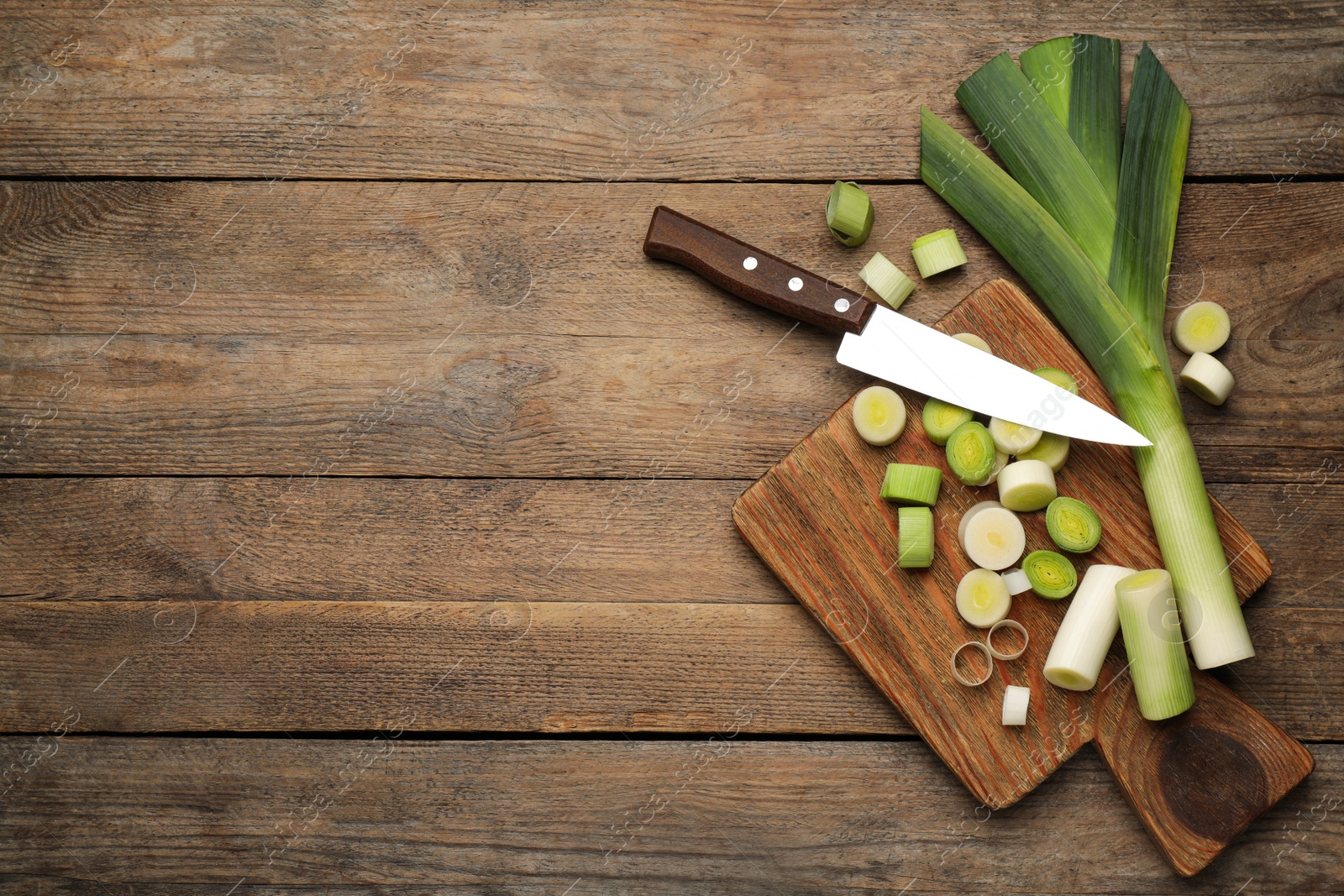 Photo of Fresh raw leeks and knife on wooden table, flat lay. Space for text