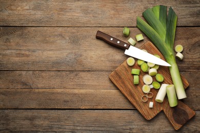 Photo of Fresh raw leeks and knife on wooden table, flat lay. Space for text