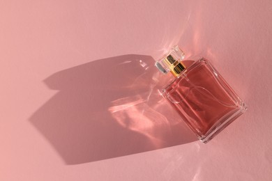 Photo of Luxury women's perfume. Sunlit glass bottle on pink background, top view. Space for text