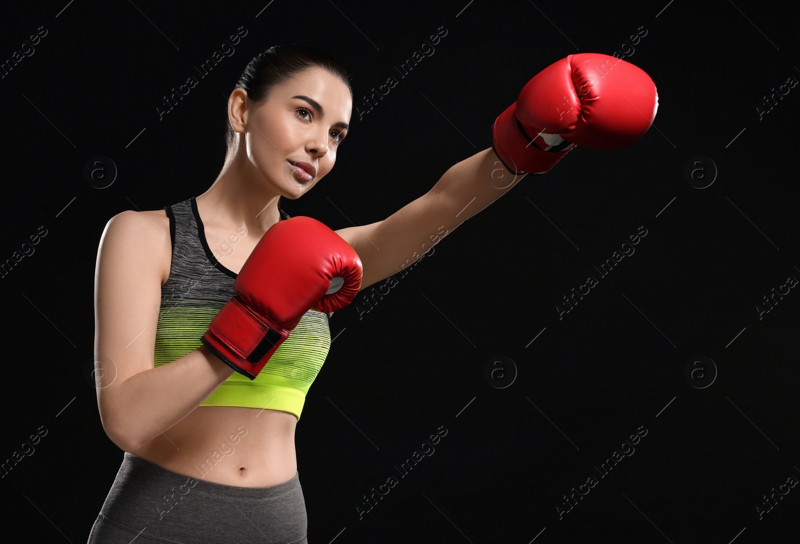 Photo of Beautiful woman in boxing gloves training on black background, low angle view