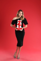 Beautiful young woman with Christmas presents on red background