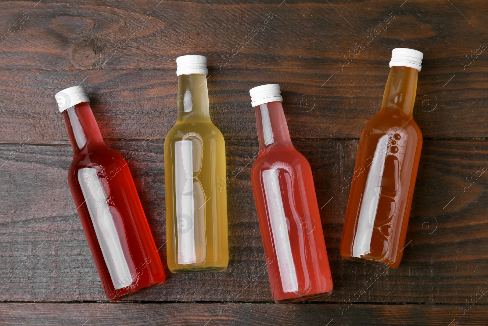 Photo of Delicious kombucha in glass bottles on wooden table, flat lay