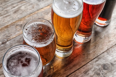 Photo of Glasses with different types of cold tasty beer on wooden table