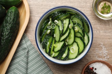 Photo of Delicious salad with cucumbers and green onion in bowl on wooden table, flat lay