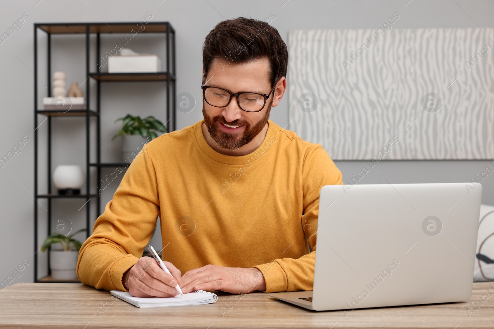 Photo of Man writing in notebook at wooden table indoors