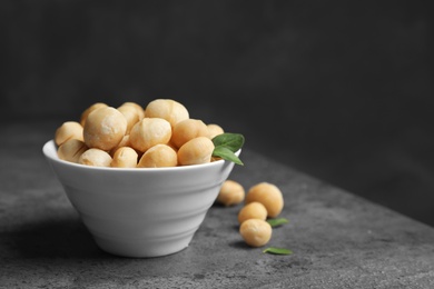Photo of Bowl with shelled organic Macadamia nuts on table against dark background. Space for text