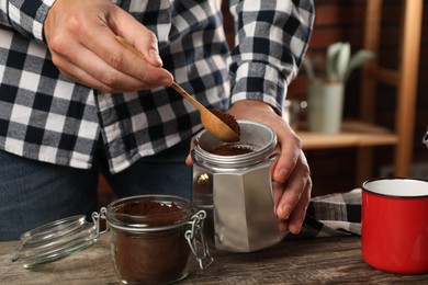 Man putting ground coffee into moka pot at table in kitchen, closeup