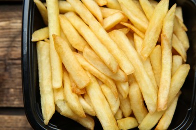 Photo of Container with French fries on wooden table, top view. Food delivery service