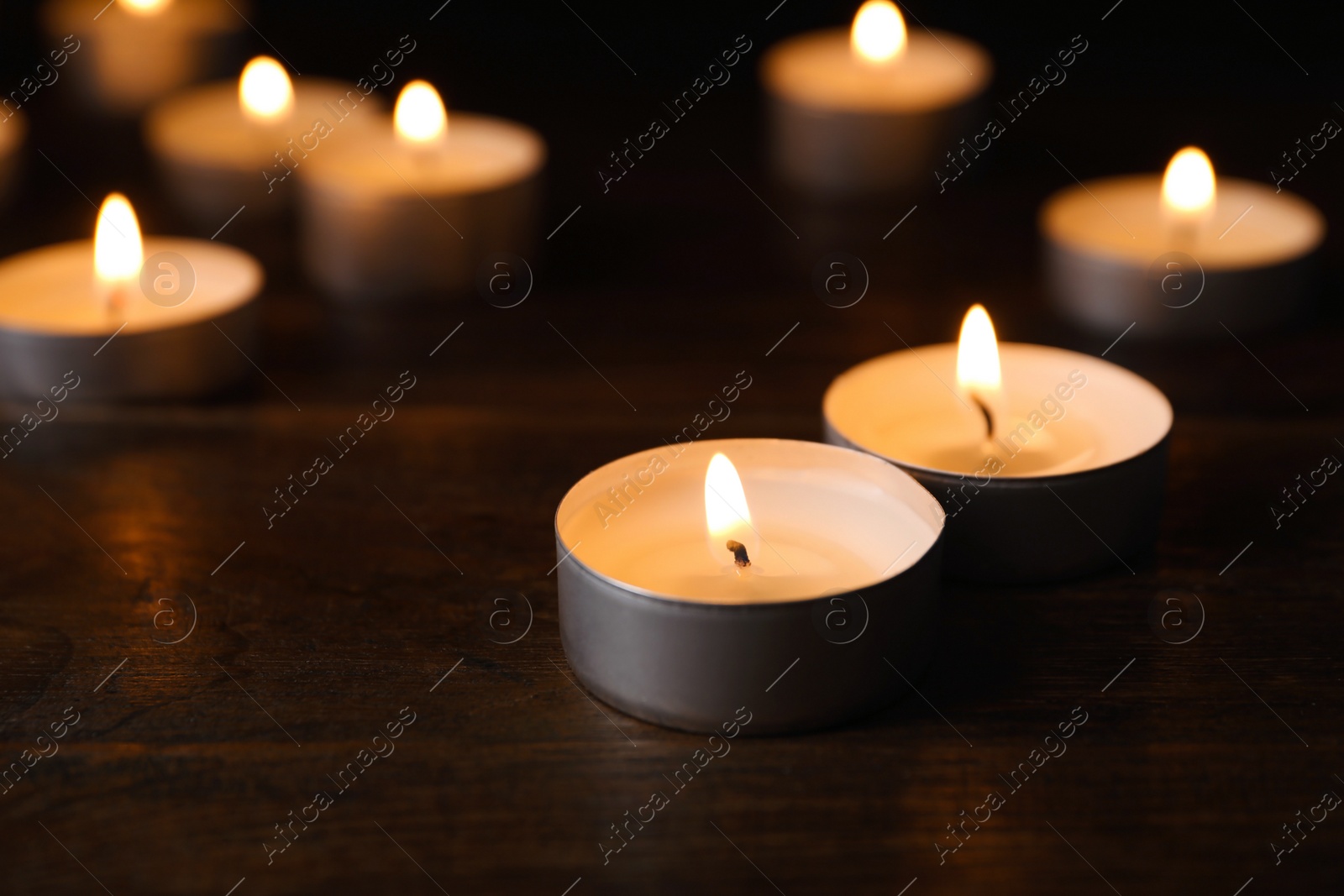 Photo of Wax candles burning on table in darkness, closeup