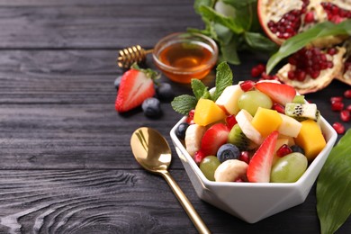 Photo of Delicious fresh fruit salad in bowl on black wooden table, space for text