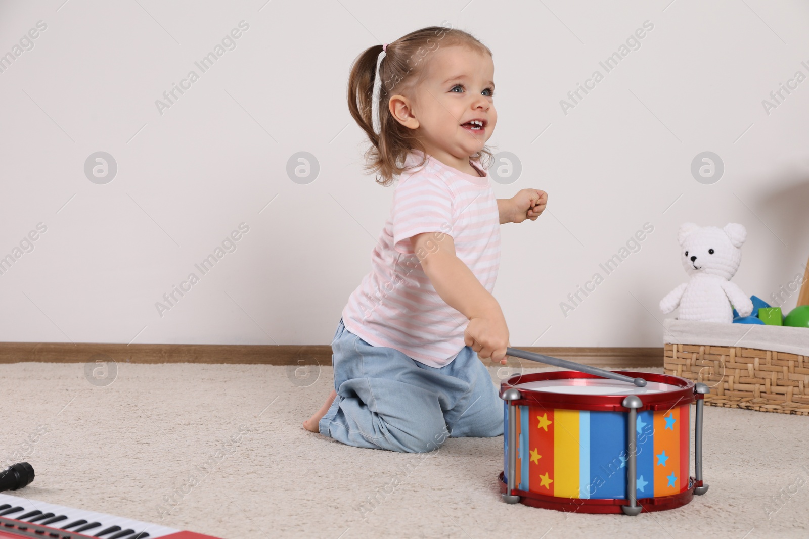 Photo of Cute little girl playing with drum and drumsticks at home, space for text