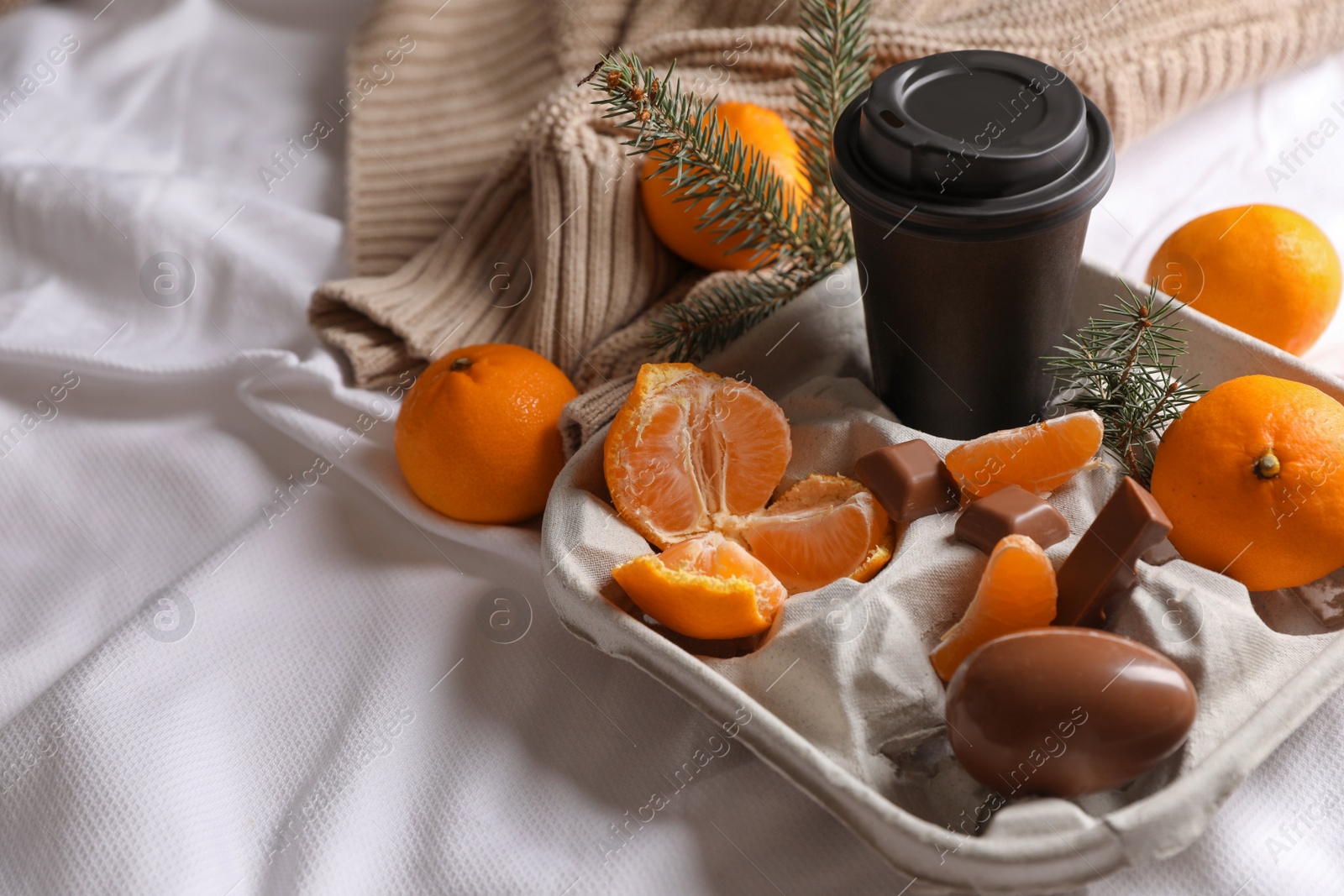 Photo of Delicious ripe tangerines, cup with drink and chocolates on white bedsheet