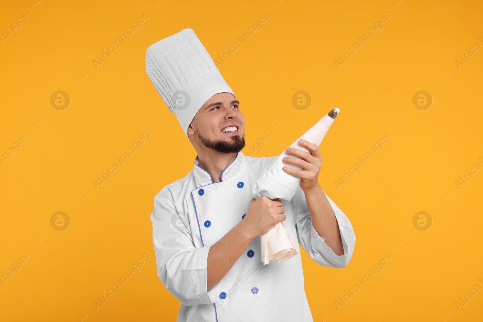 Photo of Happy professional confectioner in uniform holding piping bag on yellow background