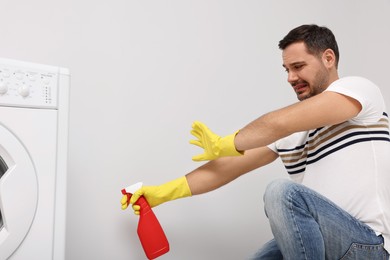Photo of Emotional man in rubber gloves cleaning wall with sprayer indoors