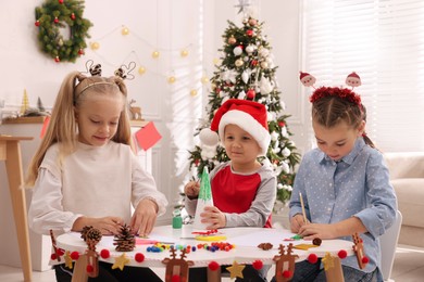 Photo of Cute little children making Christmas crafts at table in decorated room