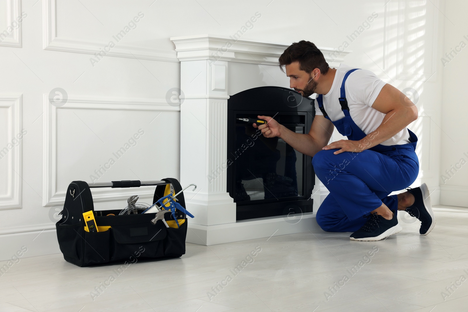 Photo of Professional technician with screwdriver installing electric fireplace in room