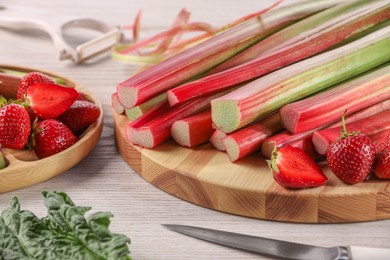 Cut fresh rhubarb stalks, strawberries and knife on white wooden table, closeup
