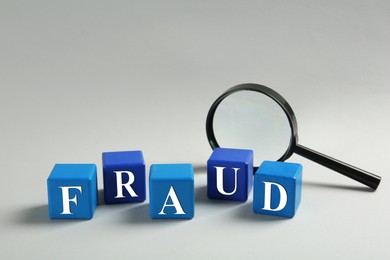 Photo of Wooden cubes with word Fraud and magnifying glass on light grey background