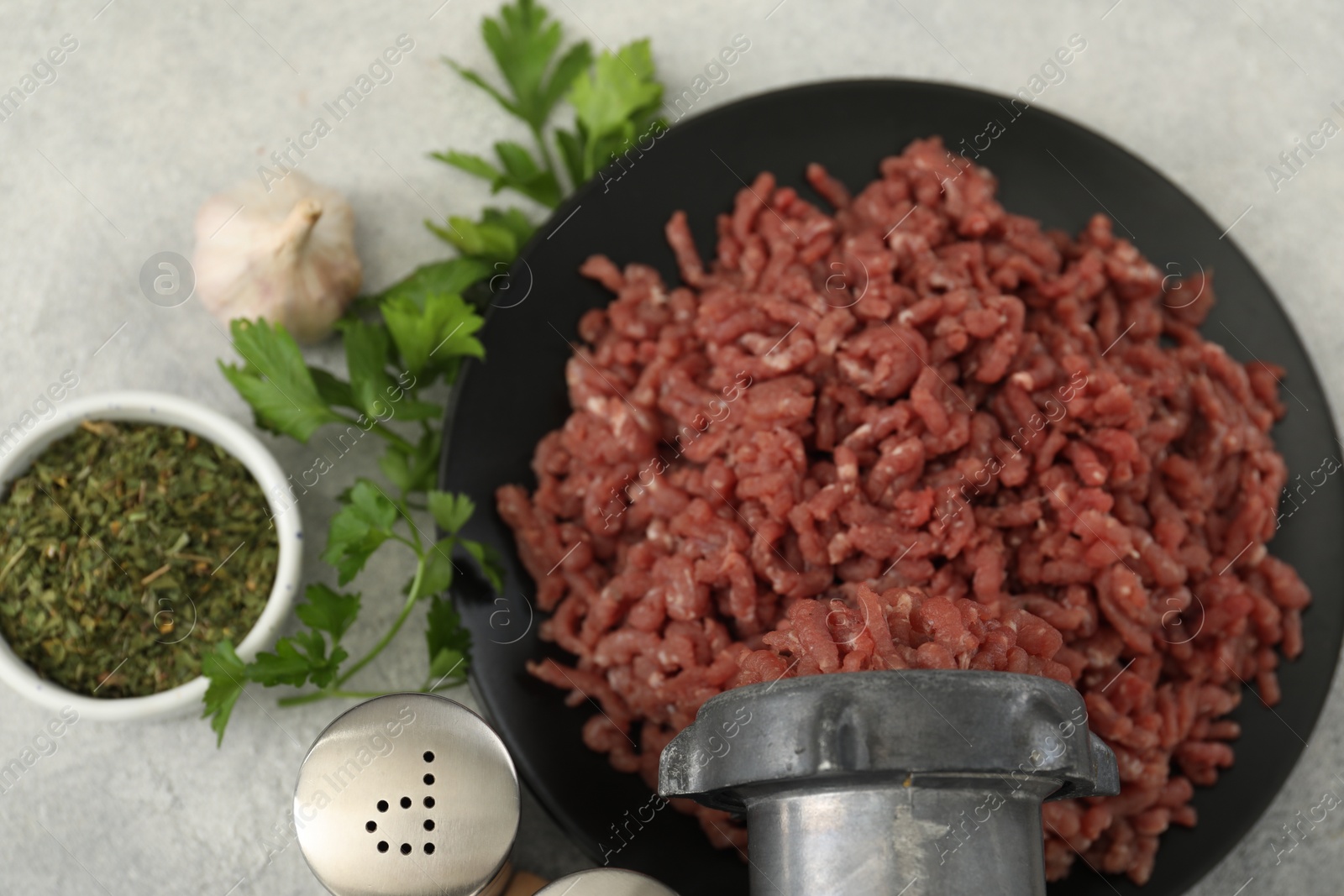 Photo of Mincing beef with meat grinder. Parsley, garlic and spices on grey table, flat lay