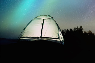 Image of Modern camping tent glowing in twilight outdoors