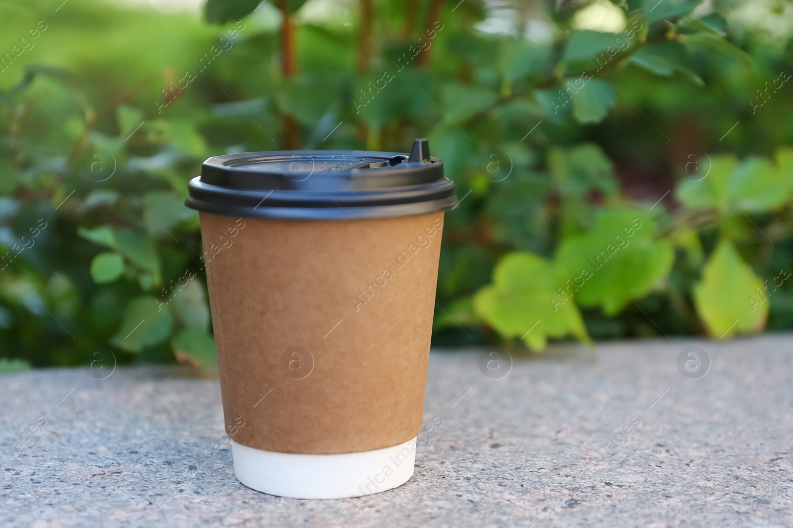 Photo of Disposable paper cup with plastic lid on stone parapet outdoors, space for text