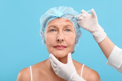 Photo of Doctor giving facial injection to senior woman on light blue background. Cosmetic surgery