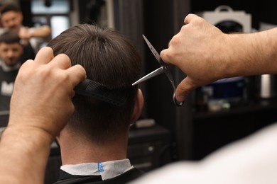 Photo of Professional hairdresser cutting man's hair in barbershop