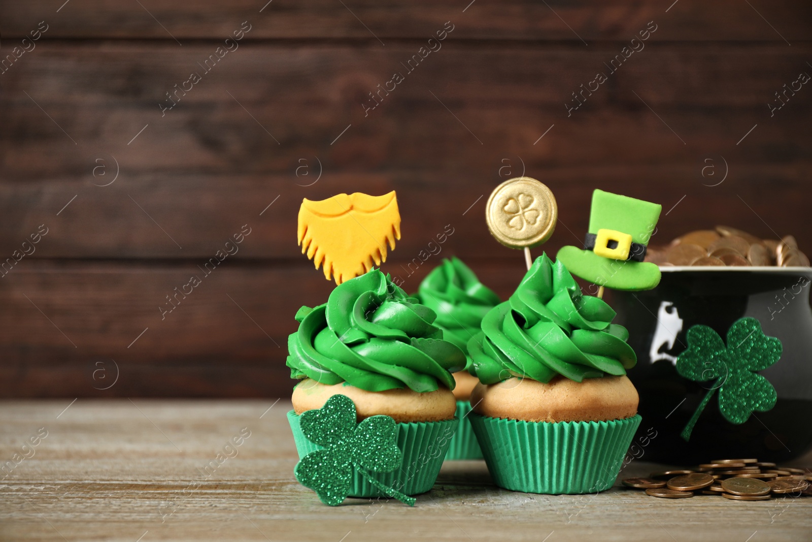 Photo of Decorated cupcakes and pot with gold coins on wooden table. St. Patrick's Day celebration