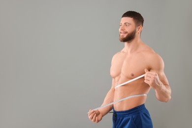 Photo of Portrait of happy athletic man measuring waist with tape on grey background, space for text. Weight loss concept