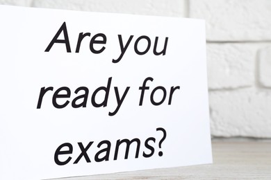Paper with question Are you ready for exams on white wooden table, closeup