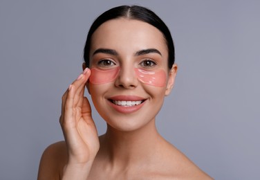 Beautiful young woman with under eye patches on grey background