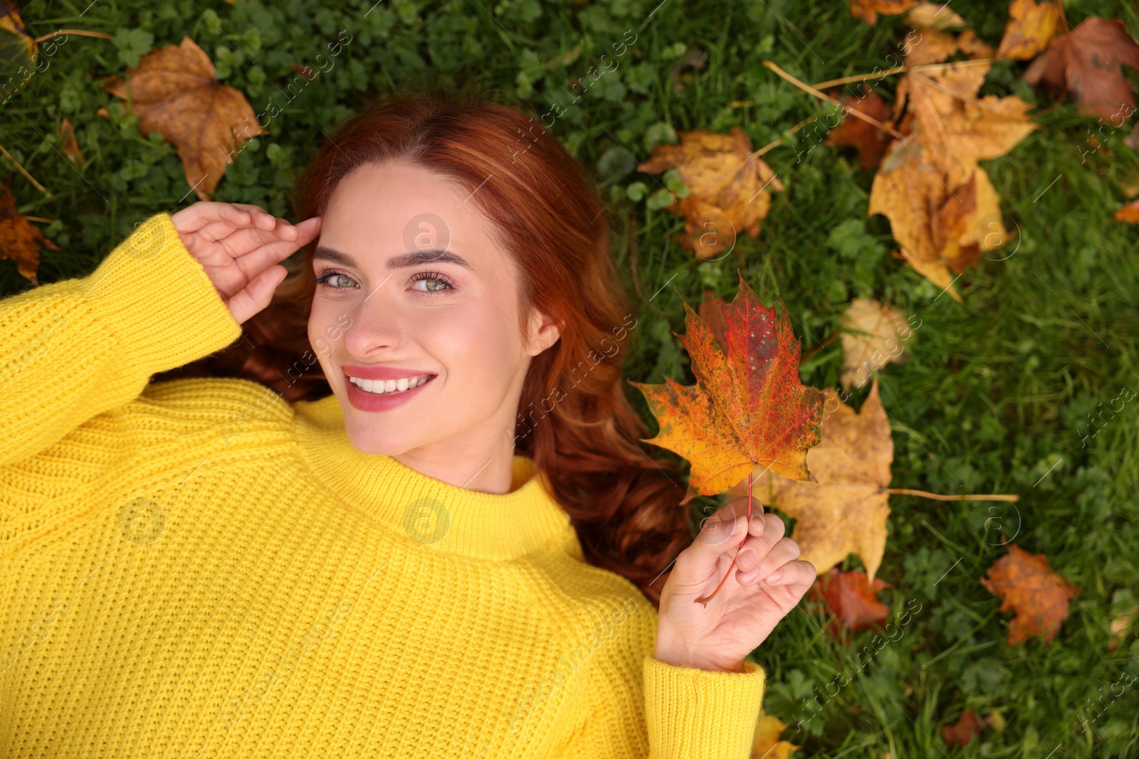 Photo of Smiling woman lying on grass among autumn leaves, top view. Space for text