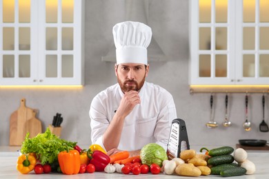 Photo of Portrait of thoughtful chef near vegetables at table in kitchen