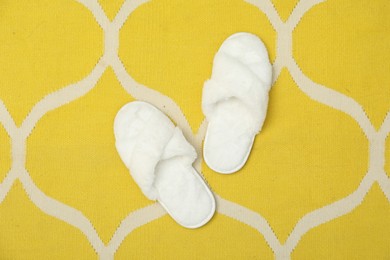 Photo of Soft fluffy white slippers on yellow carpet, top view