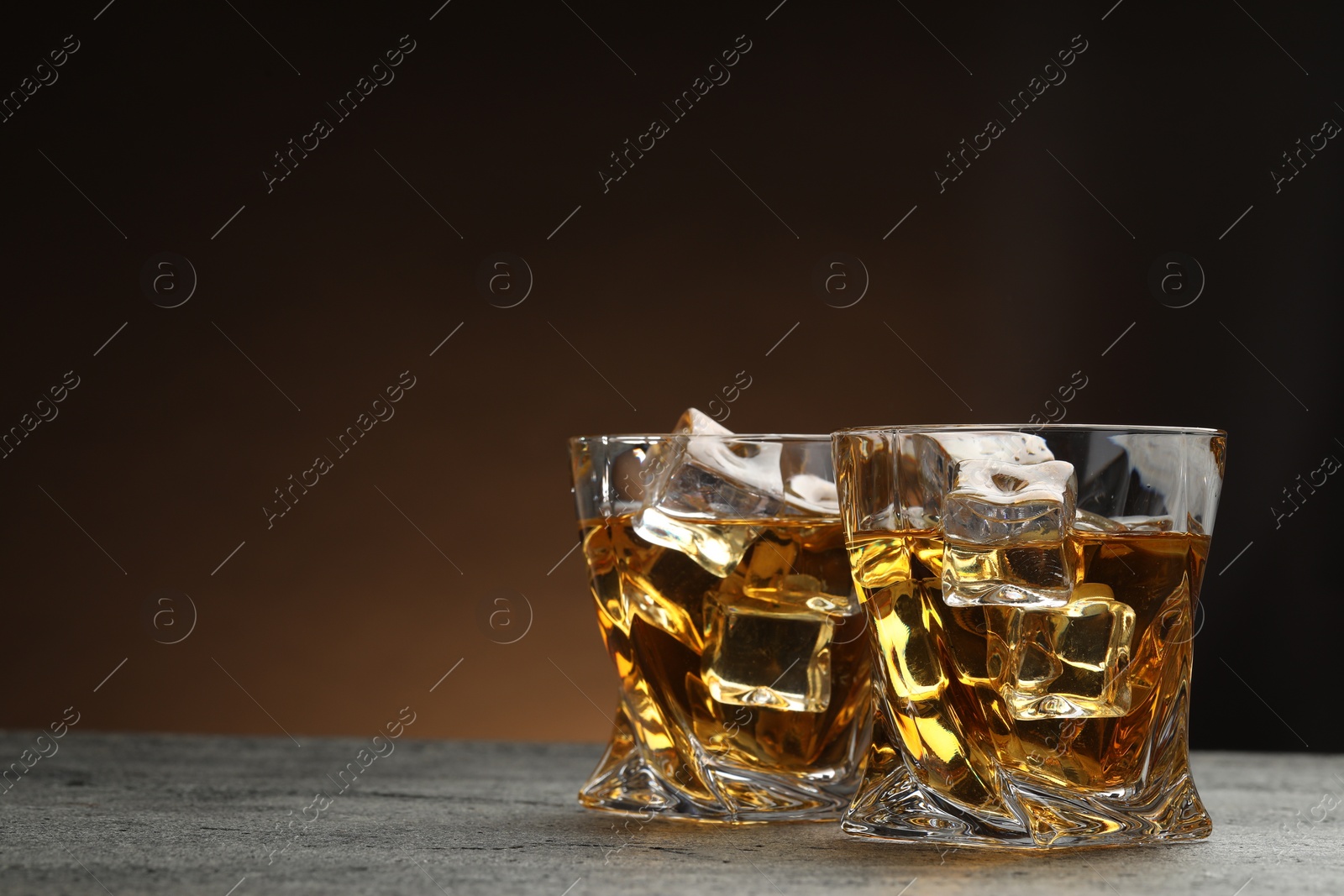 Photo of Whiskey and ice cubes in glasses on grey textured table, closeup. Space for text