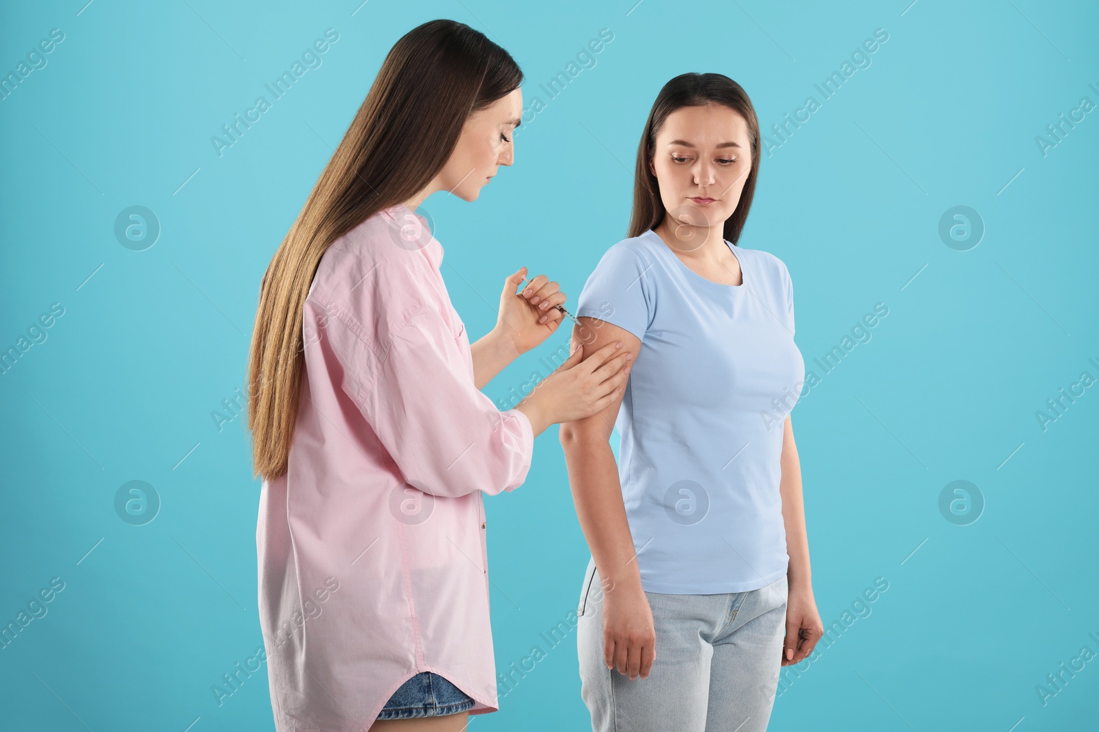 Photo of Woman giving insulin injection to her diabetic friend on light blue background