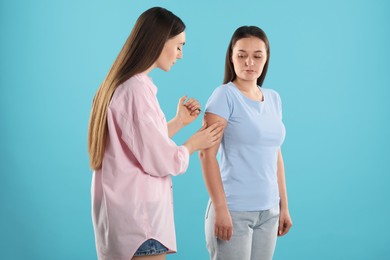 Woman giving insulin injection to her diabetic friend on light blue background