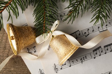 Photo of Bells, fir branches and music sheets on wooden table, closeup. Christmas decor